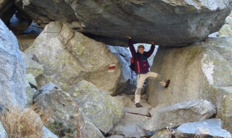 Auszeit für Angehörige Eine Person steht unter einem Felsen auf einem Wanderweg. Die Arme nach oben gestemmt, als ob sie den Felsen hochhalten würde.